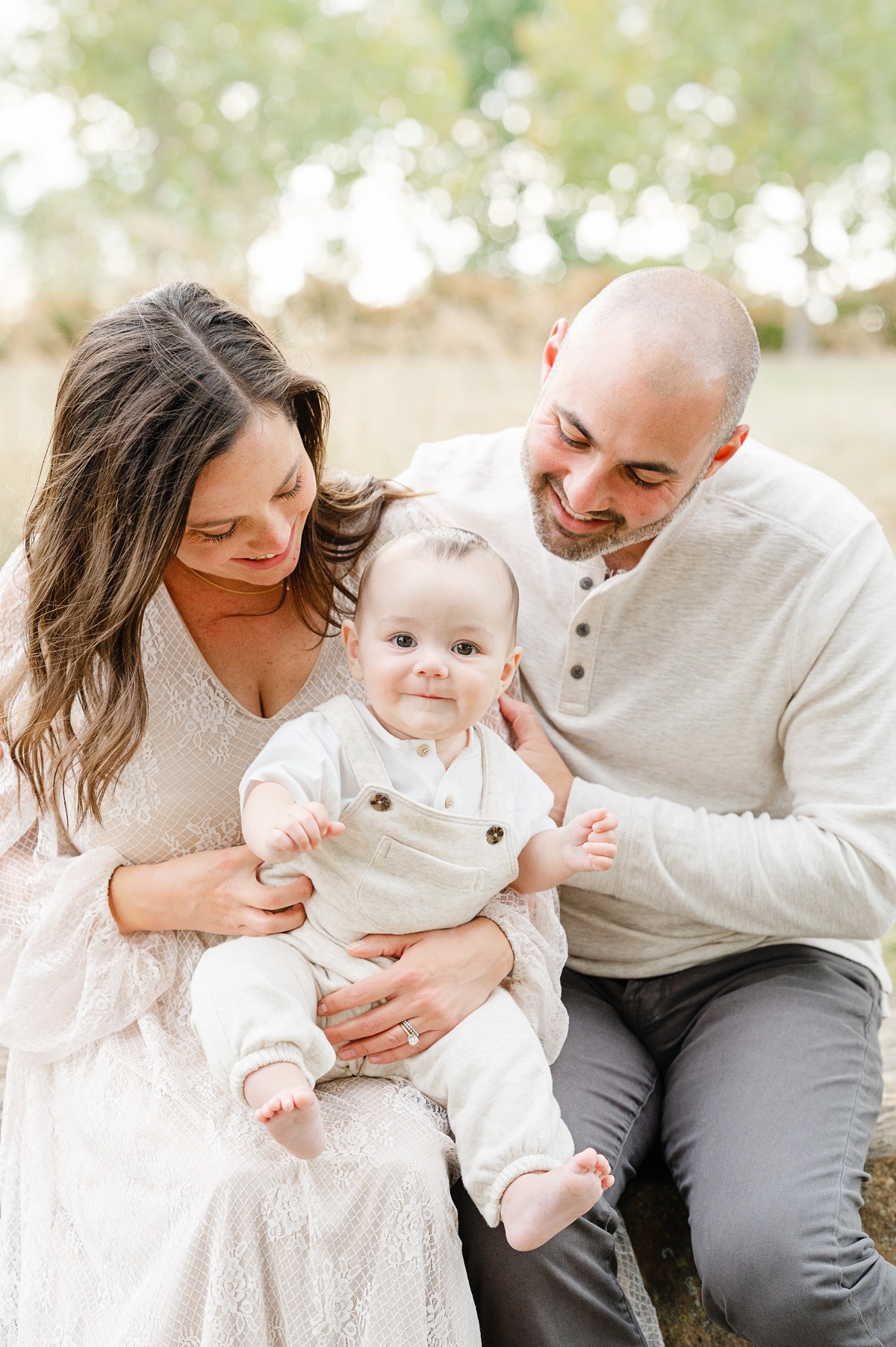 family portrait of mom and dad looking at their baby in a park.